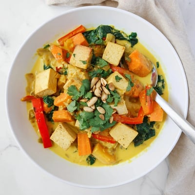 Aromatic vegetarian pumpkin tofu curry served in a bowl topped with vibrant cilantro and toasted pumpkin seeds.