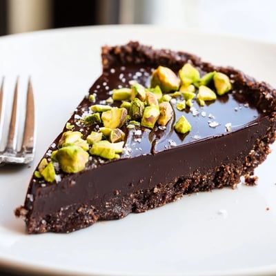 Glossy dark chocolate pistachio tart with a crumbly cocoa crust finished with flaky sea salt
