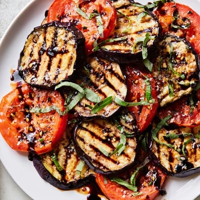 Grilled tomato eggplant with charred edges drizzled in balsamic glaze served warm