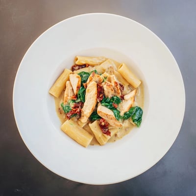 Rich one pan Tuscan chicken pasta served hot with wilted spinach and Parmesan.  